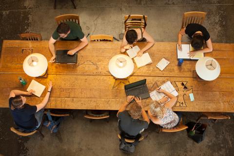 A birds-eye view of students studying individually at a long desk or work table.